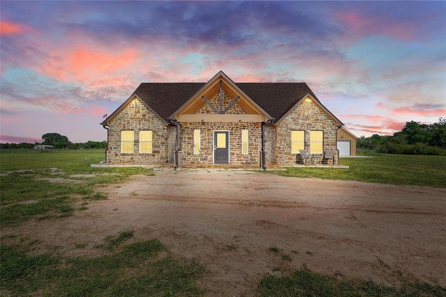 Craftsman-style house featuring stone siding, a lawn, roof with shingles, and dirt driveway Craftsman-style house featuring stone siding, a lawn, roof with shingles, and dirt driveway