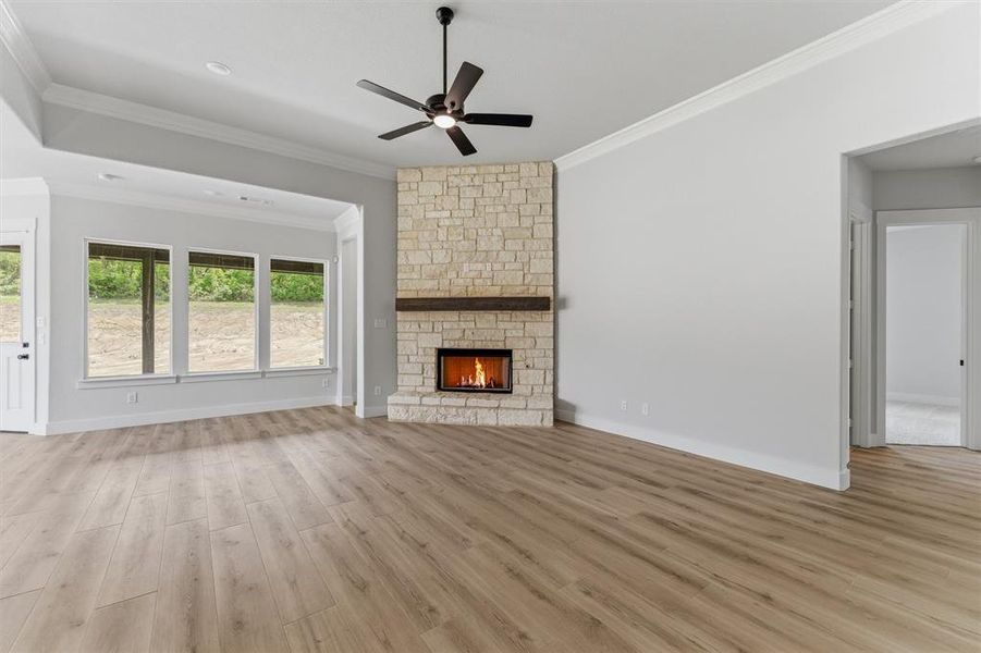 Unfurnished living room with light wood-type flooring, a ceiling fan, ornamental molding, and a fireplace