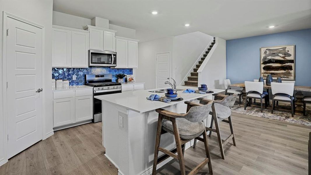 Kitchen featuring stainless steel appliances, white cabinets, a kitchen bar, a kitchen island with sink, and light wood-type flooring
