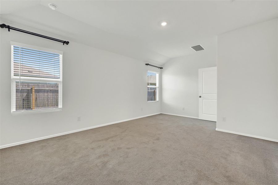A spacious, naturally illuminated room features light gray carpeting and white walls, offering a versatile living space.