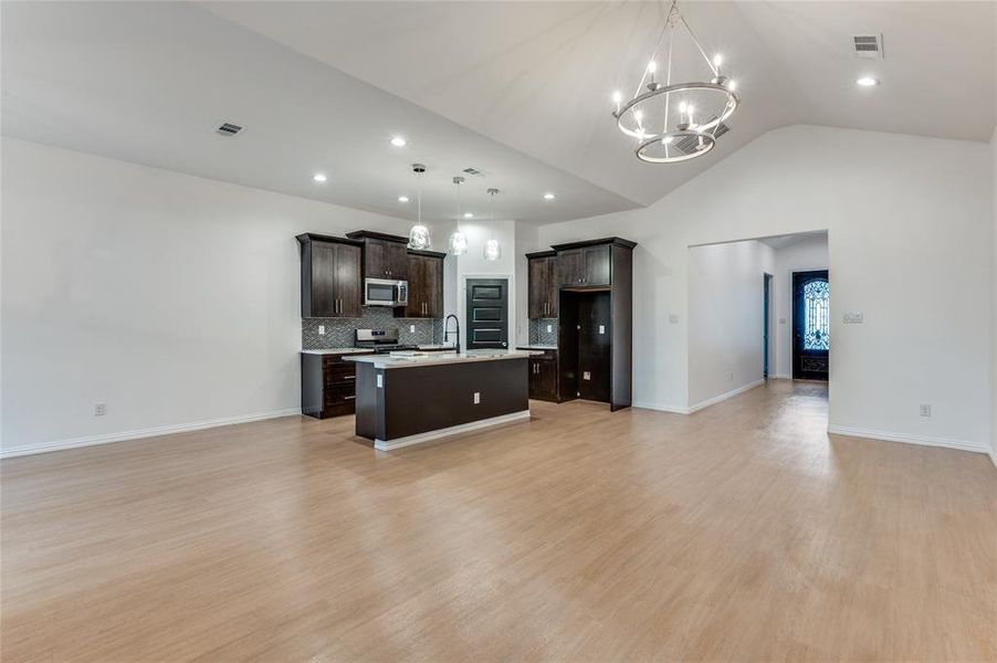 Kitchen with light wood-type flooring, decorative light fixtures, appliances with stainless steel finishes, dark brown cabinets, and a center island with sink