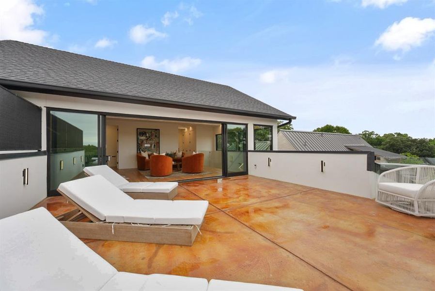 Expansive rooftop deck featuring stained concrete flooring, a partial privacy wall with integrated lighting, and direct access to an interior space through large sliding glass doors