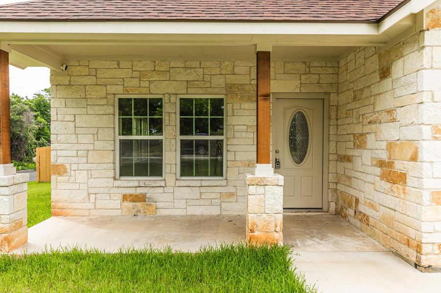 View of exterior entry with a shingled roof and stone siding