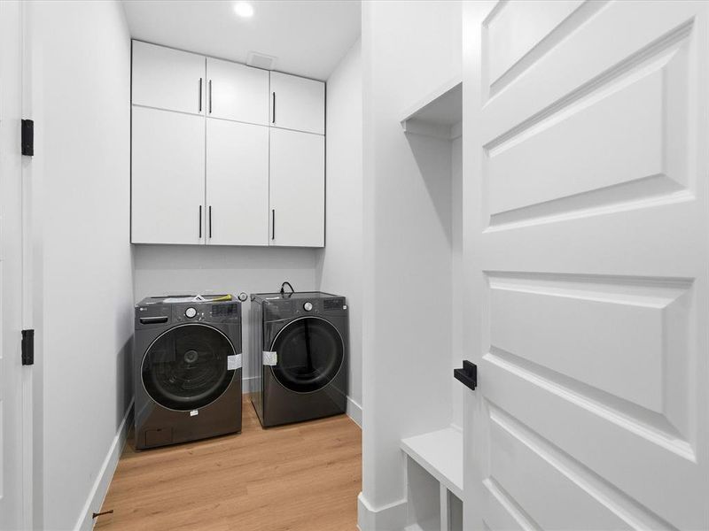 Dedicated laundry space featuring wood-finish flooring, white flat-panel cabinetry with dark hardware, and recessed lighting