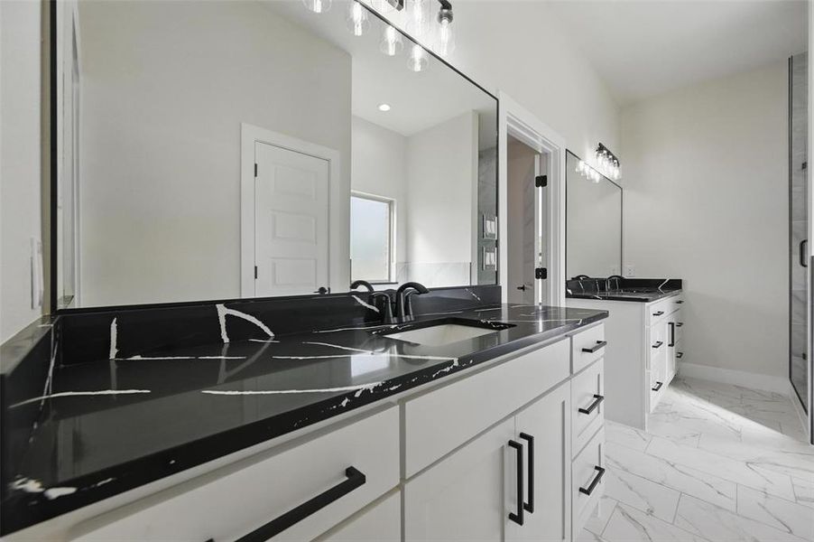 Bathroom featuring marble look tiles, two vanities, baseboards, and a shower stall Bathroom featuring marble look tiles, two vanities, baseboards, and a shower stall