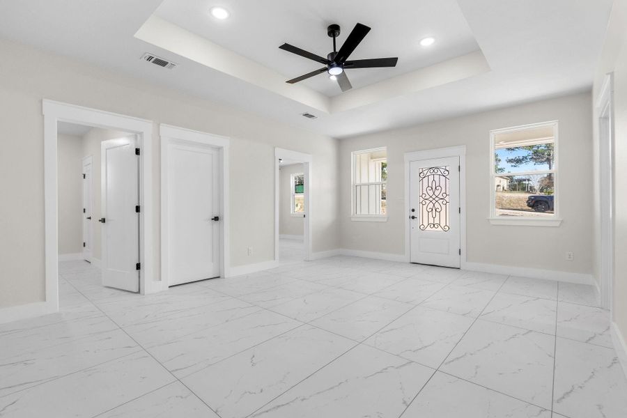 Entryway way to living room with access to both bedroom with ceiling fan and a raised trey ceiling