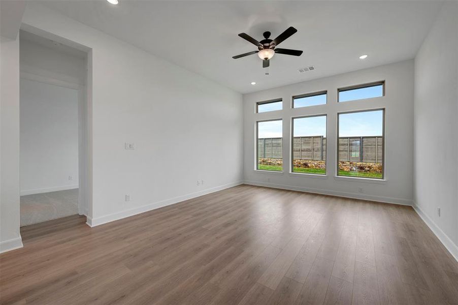 Spacious room featuring light wood flooring, a ceiling fan with integrated lighting, recessed lighting, and large windows offering exterior views