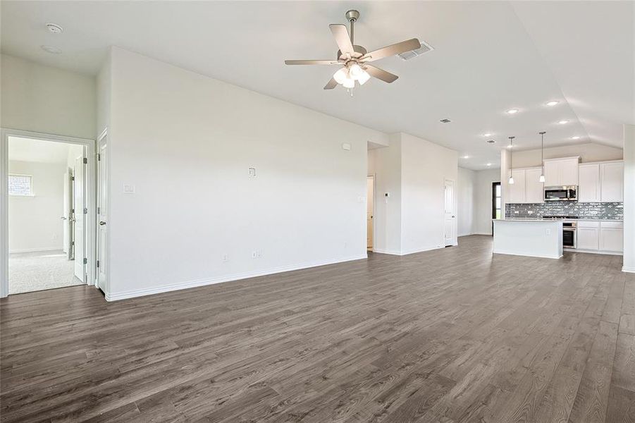 Unfurnished living room with ceiling fan, vaulted ceiling, and dark wood-type flooring