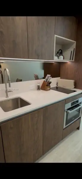 Wood-finish cabinetry, solid-surface countertops, undermount stainless steel sink, built-in cooktop, and integrated wall oven