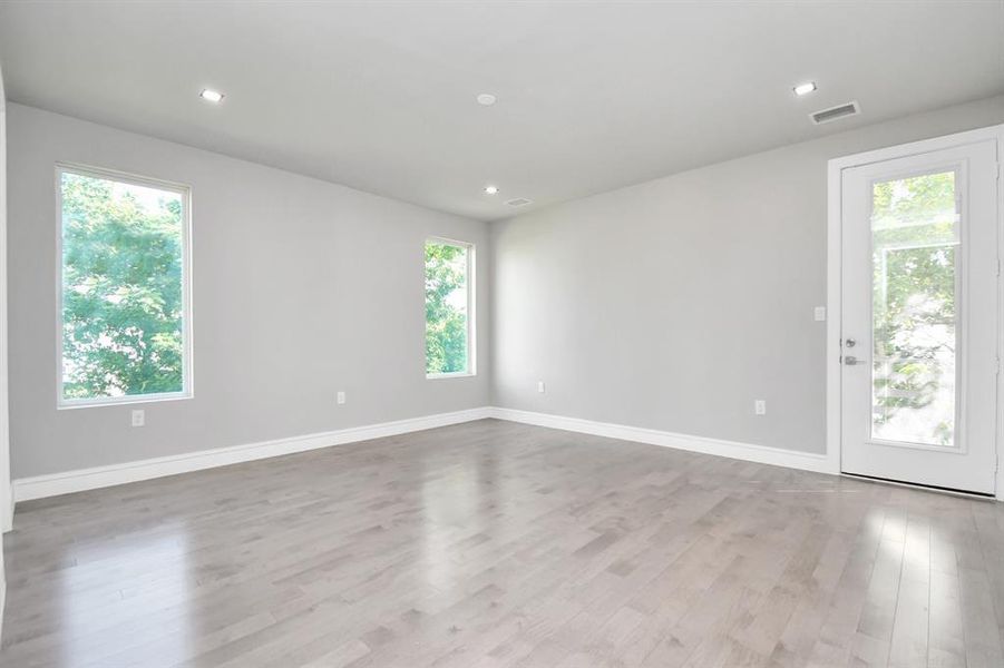 This is a modern, bright room with light grey walls, recessed lighting, and sleek hardwood floors. It features a large mirrored closet, two white doors, and an open doorway leading to another room, suggesting a spacious layout.