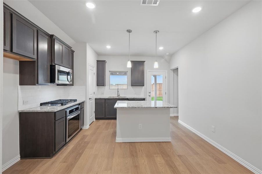 Kitchen featuring decorative backsplash, a center island, light wood-style flooring, pendant lighting, and stainless steel appliances