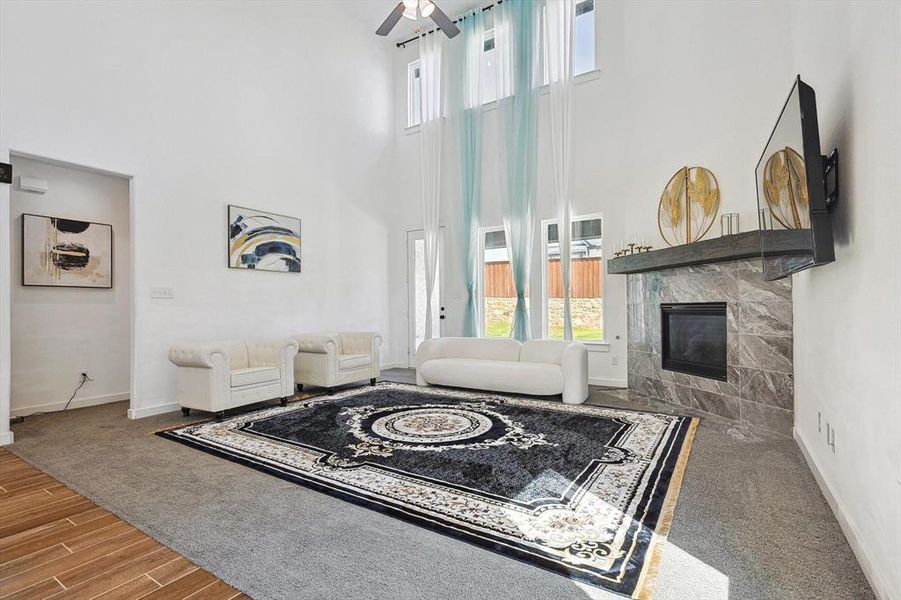 Living room featuring ceiling fan, hardwood / wood-style flooring, a fireplace, and a towering ceiling