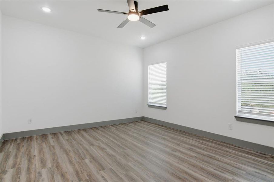 Spacious room featuring wood-finish flooring, white walls, and a contemporary ceiling fan