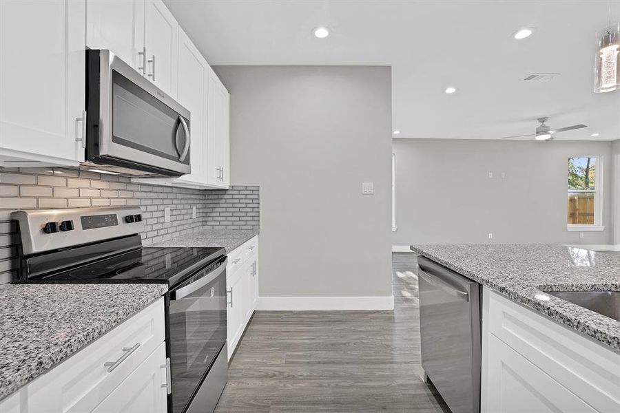 Kitchen featuring white cabinetry, ceiling fan, light stone counters, wood-type flooring, and appliances with stainless steel finishes