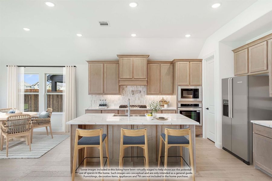 Kitchen with light wood cabinets, large island with seating, stainless steel appliances, and open dining area nearby.