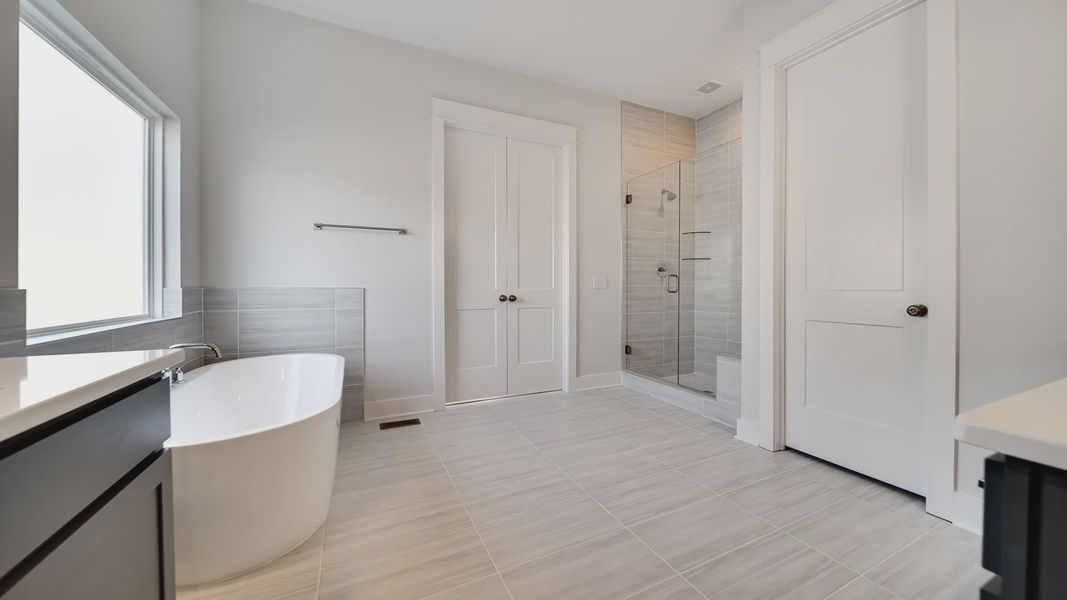 Large tiled bathroom with multiple vanities, glass shower enclosure, and freestanding tub