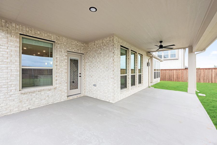 Covered back patio with ceiling fan, concrete floor, brick exterior, and fenced backyard with green lawn