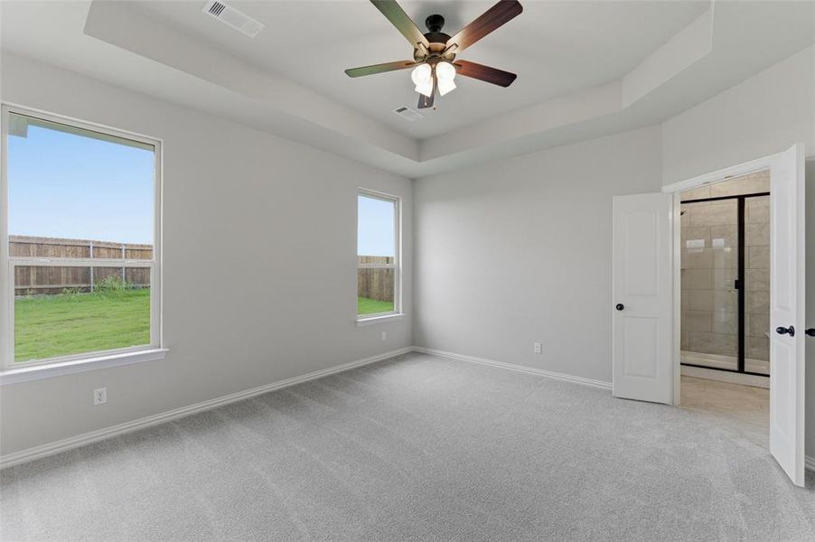 Spacious room featuring light gray carpet flooring, two windows with backyard views, and a tray ceiling with a ceiling fan