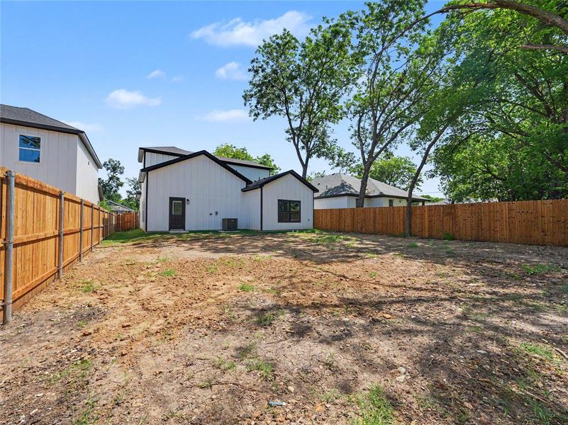 Expansive backyard space featuring natural fencing and a two-story residence with dark trim Expansive backyard space featuring natural fencing and a two-story residence with dark trim