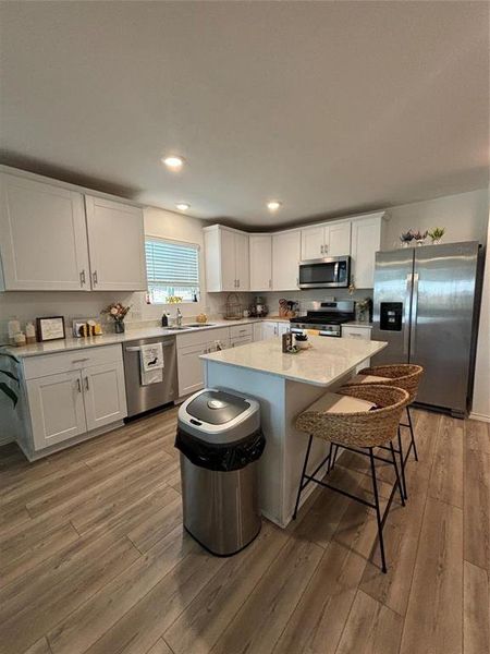 Kitchen with appliances with stainless steel finishes, white cabinets, a breakfast bar area, light wood-type flooring, and a kitchen island