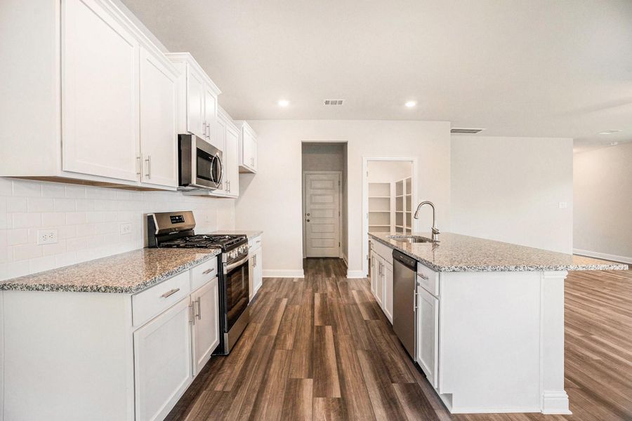 Modern kitchen with sleek white cabinets, granite countertops, and stainless steel appliances. Features a spacious island with a sink, open layout, and luxury vinyl plank flooring.