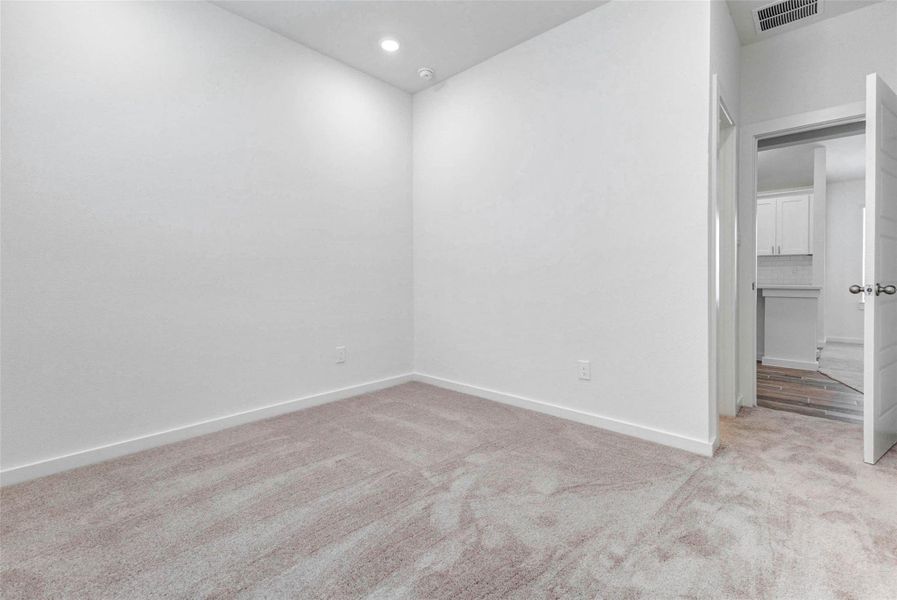 This secondary bedroom offers soft carpet, tall ceilings, recessed lighting, and a simple neutral design that can easily work as a guest room, office, nursery, or flex space. The nearby doorway provides convenient access back toward the main living areas and kitchen. This secondary bedroom offers soft carpet, tall ceilings, recessed lighting, and a simple neutral design that can easily work as a guest room, office, nursery, or flex space. The nearby doorway provides convenient access back toward the main living areas and kitchen.
