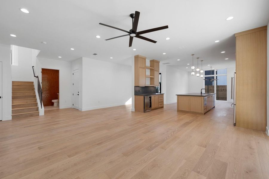 Unfurnished living room with stairway, light wood finished floors, recessed lighting, a ceiling fan, and beverage cooler Unfurnished living room with stairway, light wood finished floors, recessed lighting, a ceiling fan, and beverage cooler