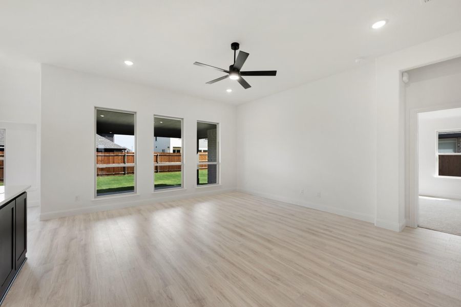 Open living room with light wood floors, black ceiling fan, and three backyard-facing windows