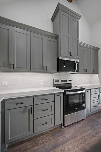 Quartz countertops and gray custom cabinets with spice rack drawer on the left of the range and a utensil drawer on the right