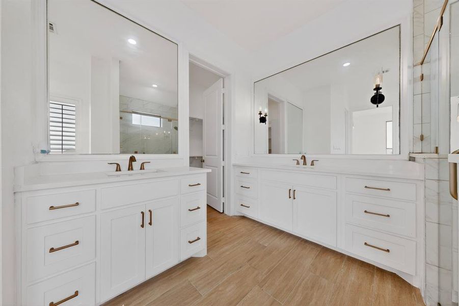 Dual white vanity cabinets with integrated sinks, quartz countertops, and bronze-finish hardware Dual white vanity cabinets with integrated sinks, quartz countertops, and bronze-finish hardware
