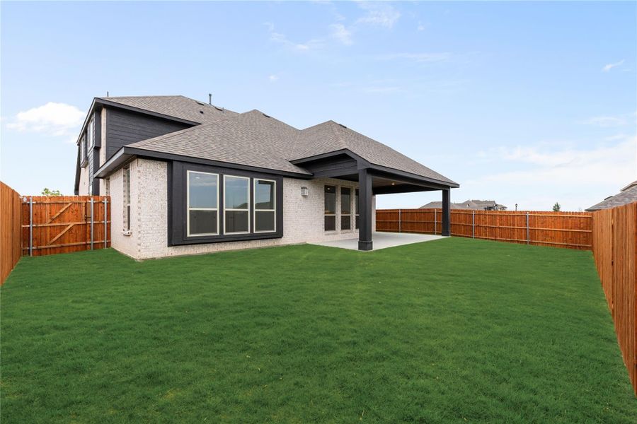 Backyard of two-story brick home with covered patio, green lawn, and wood privacy fence. Backyard of two-story brick home with covered patio, green lawn, and wood privacy fence.