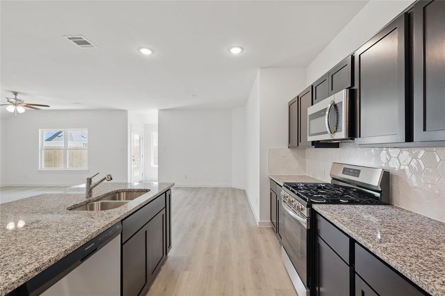 Kitchen with appliances with stainless steel finishes, light stone counters, light wood finished floors, open floor plan, and decorative backsplash