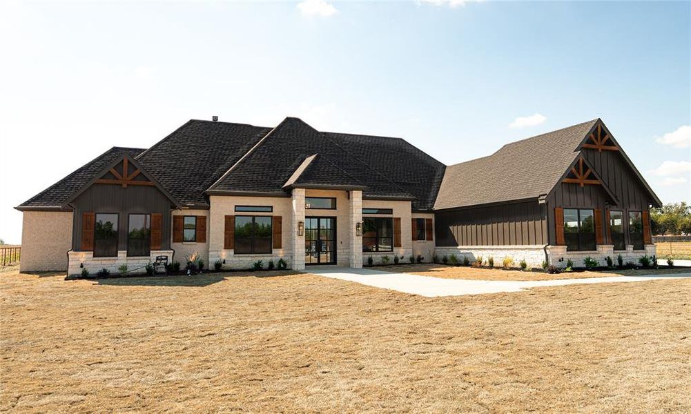 Modern inspired farmhouse featuring stone siding, board and batten siding, and a shingled roof