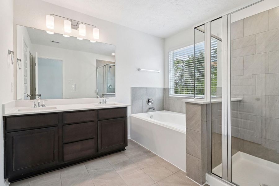 This beautiful primary bathroom is move-in ready! It showcases stained cabinetry paired with light countertops, dual vanity sinks, a large mirror, high ceilings, custom paint, soaking tub, walk-in shower, and stylish modern finishes throughout.
