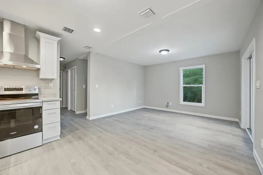 Kitchen featuring stainless steel range, professional-grade range hood, white cabinetry, and wood-finish flooring Kitchen featuring stainless steel range, professional-grade range hood, white cabinetry, and wood-finish flooring