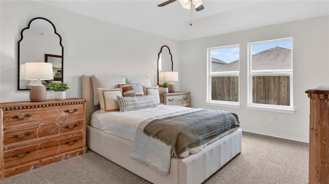 Carpeted bedroom featuring two large windows, a ceiling fan with integrated lighting, and neutral wall tones Carpeted bedroom featuring two large windows, a ceiling fan with integrated lighting, and neutral wall tones