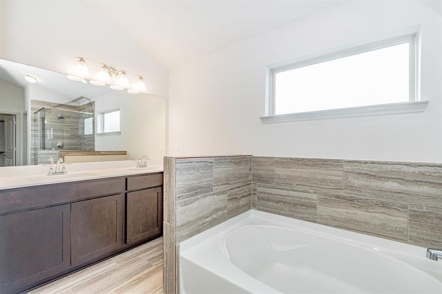 Indulge in the spa-like ambiance of this exquisite primary bathroom. Featuring dual vanities, a deep soaking tub with tile surround, and a glass-enclosed walk-in shower, this bathroom offers both style and convenience. The large mirror and modern lighting complete the sophisticated look.