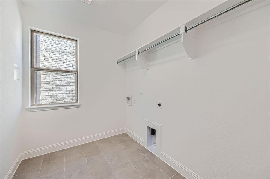 Utility room featuring tile flooring, a window with exterior brick detail, white baseboards, and a built-in hanging rod with shelving Utility room featuring tile flooring, a window with exterior brick detail, white baseboards, and a built-in hanging rod with shelving