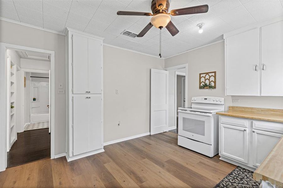 Kitchen with white cabinets, white electric stove, light countertops, light wood-type flooring, and ornamental molding