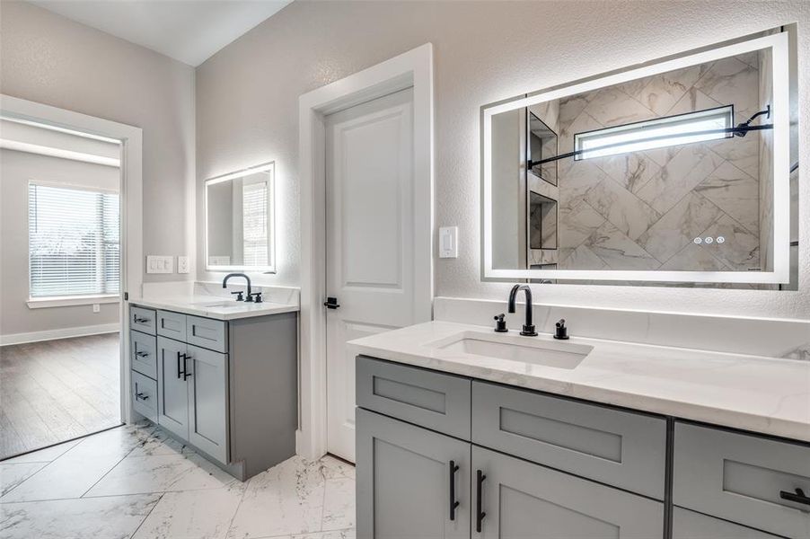 Bathroom featuring plenty of natural light, light marble finish floors, two vanities, and a textured wall