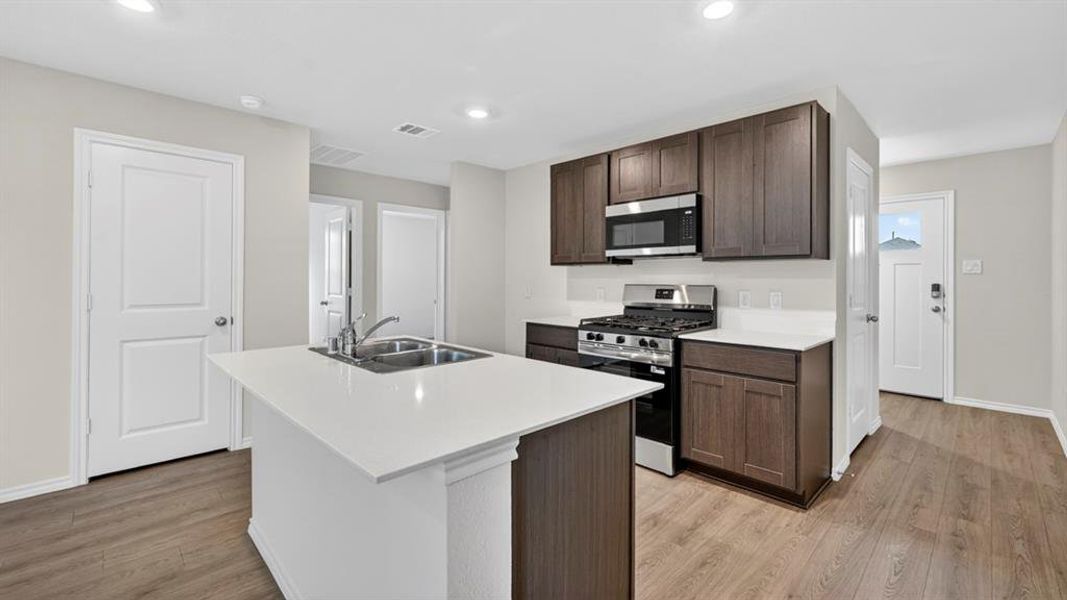 Modern kitchen featuring a central island with a double basin sink, white countertops, dark wood-finish cabinetry, and stainless steel appliances