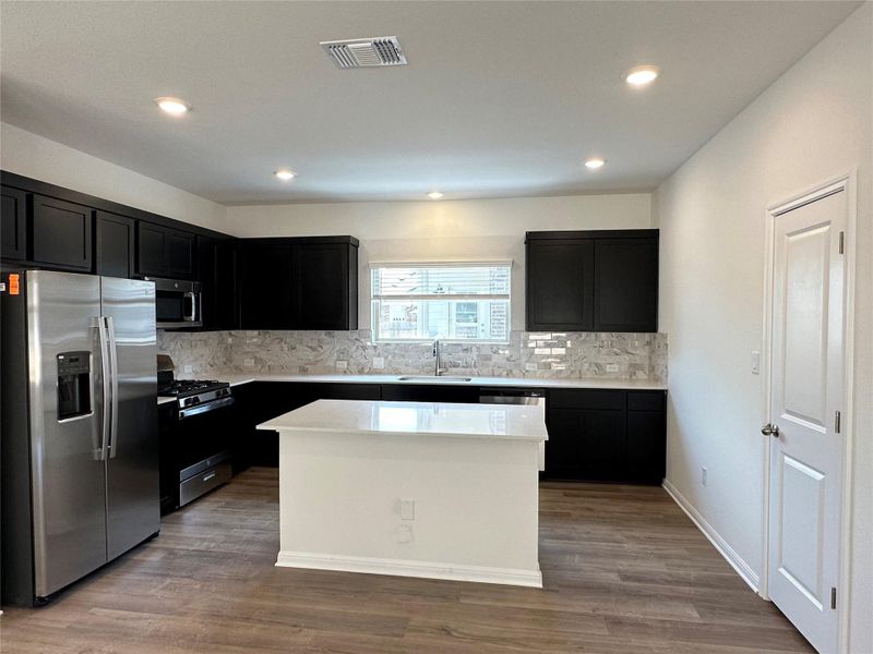 Kitchen with dark cabinetry, stainless steel appliances, dark wood finished floors, decorative backsplash, and recessed lighting