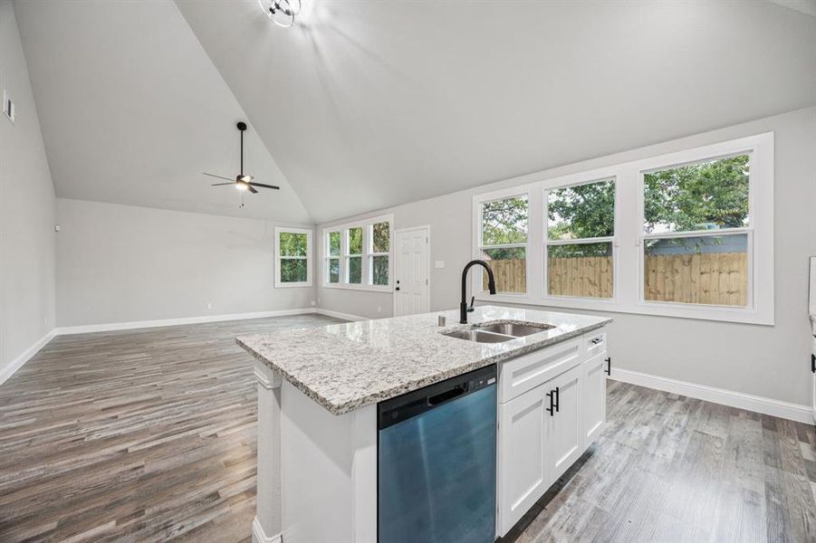 Kitchen with dishwashing machine, white cabinetry, light stone countertops, light wood-type flooring, and high vaulted ceiling