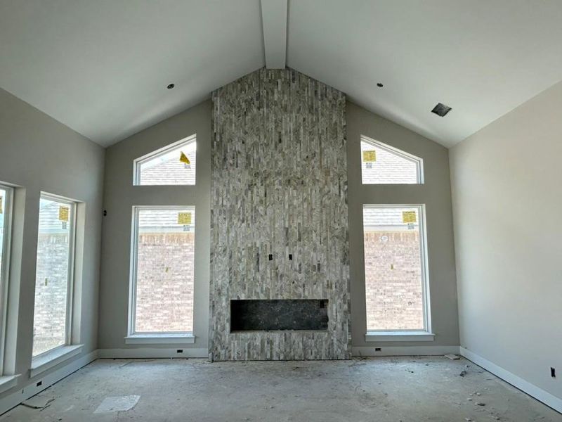 Unfurnished living room with a large fireplace, high vaulted ceiling, and unfinished concrete flooring