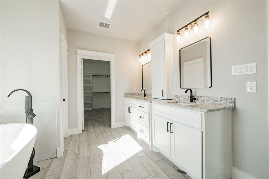 Primary bathroom with a stand-alone tub, dual vanity, a spacious closet, and wood tiled floors Primary bathroom with a stand-alone tub, dual vanity, a spacious closet, and wood tiled floors