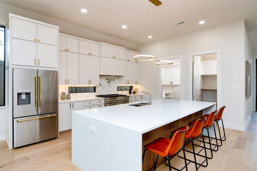 Kitchen with white cabinets, premium appliances, hanging light fixtures, and an island with sink