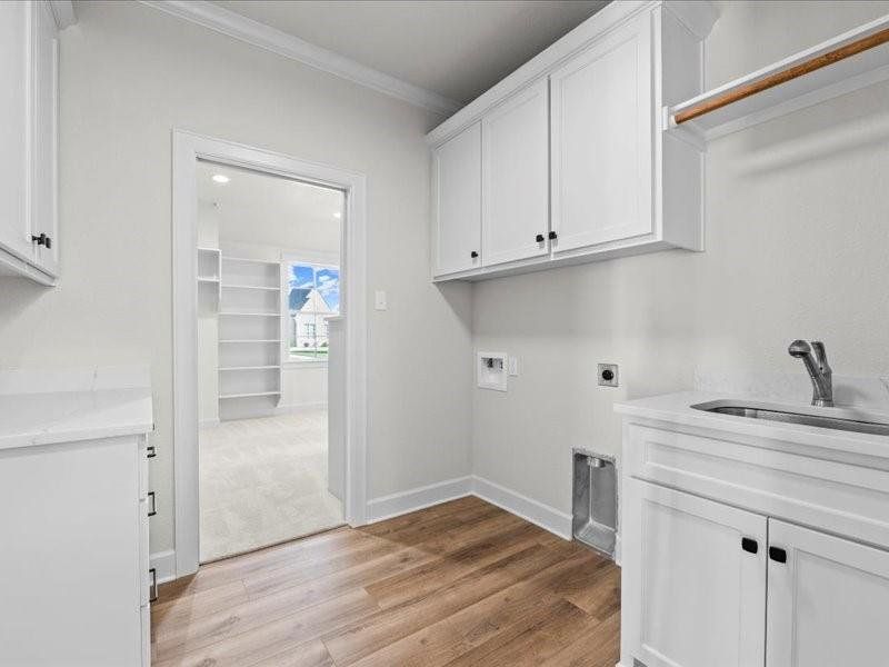 Laundry room featuring cabinet space, electric dryer hookup, light wood-style flooring, ornamental molding, and washer hookup Laundry room featuring cabinet space, electric dryer hookup, light wood-style flooring, ornamental molding, and washer hookup
