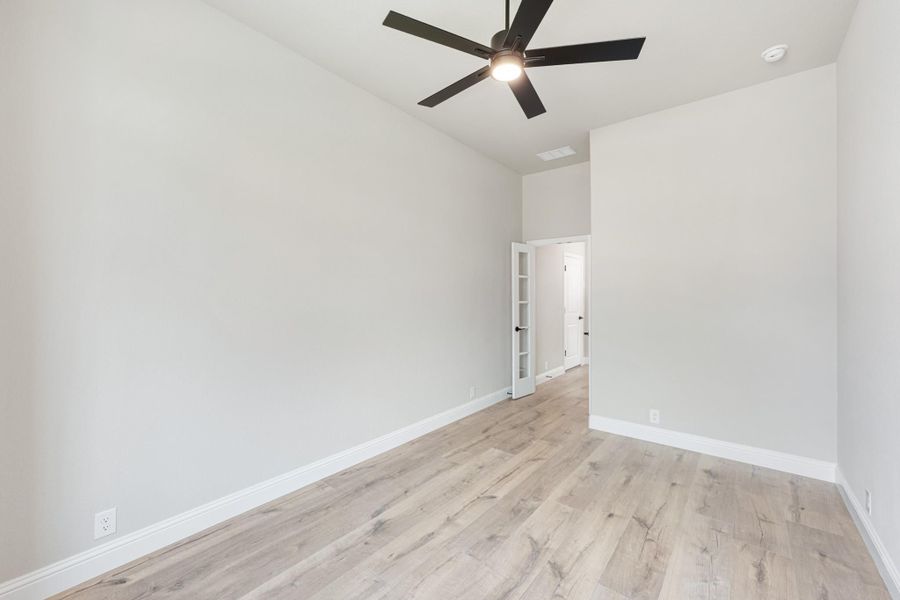 Empty bedroom with light wood floors, white walls, and a black ceiling fan