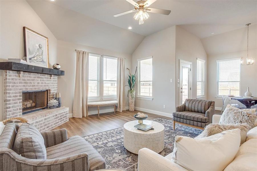 Living room featuring ceiling fan with notable chandelier, vaulted ceiling, hardwood / wood-style flooring, and a fireplace