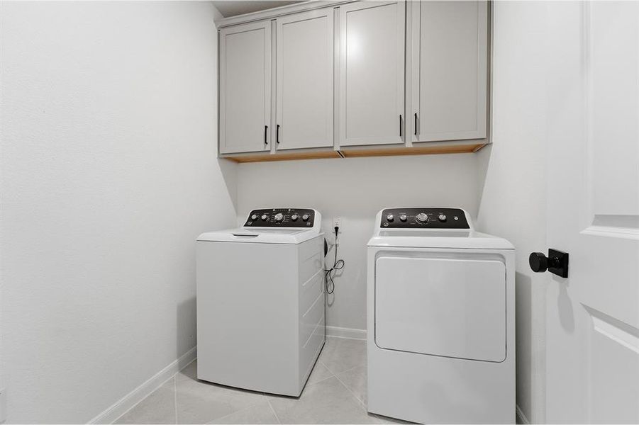 Laundry area featuring light gray cabinetry with black hardware, white walls, and light gray floor tiling
